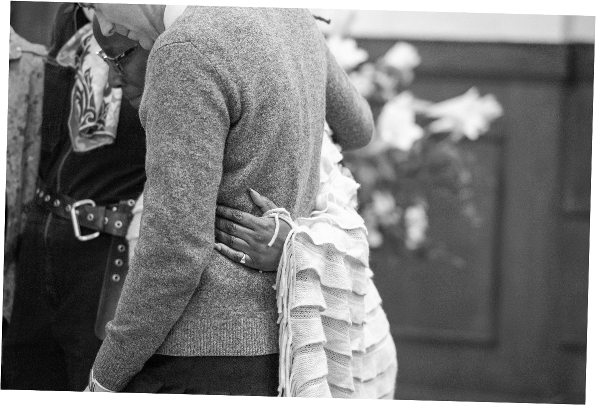 people stand holding each other at a funeral